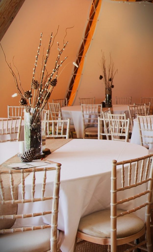 Furniture hire for events - round tables with ice white linen and beige cheesecloth. Flowers centrepiece with ambient orange lighting