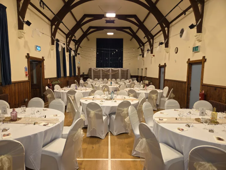 Indoor wedding reception with round tables and covered chairs in white tablecloths