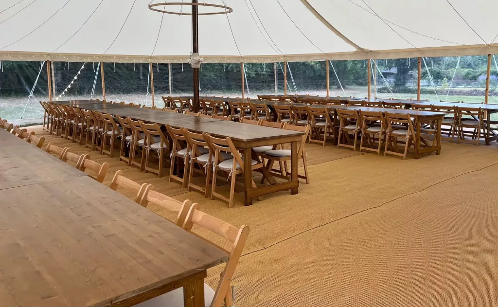 Wooden folding chairs with tie-on seat pads and rustic tables inside a marquee wedding