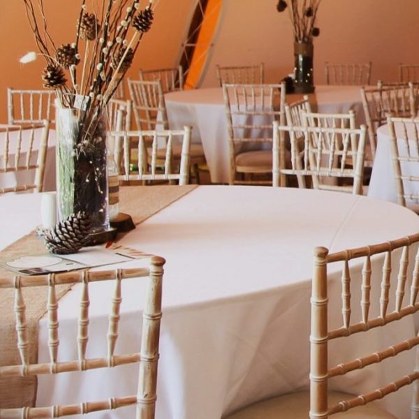 Furniture hire for events - round tables with ice white linen and beige cheesecloth. Flowers centrepiece with ambient orange lighting